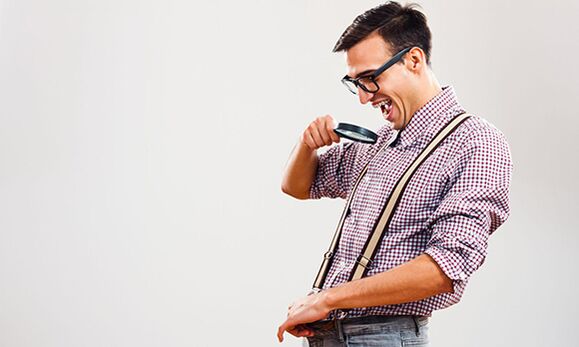 A man looks through a magnifying glass at his penis with a desire to increase its size